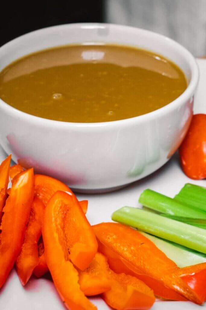 date syrup Vinaigrette in a white bowl next to chopped raw veggies on a white plate