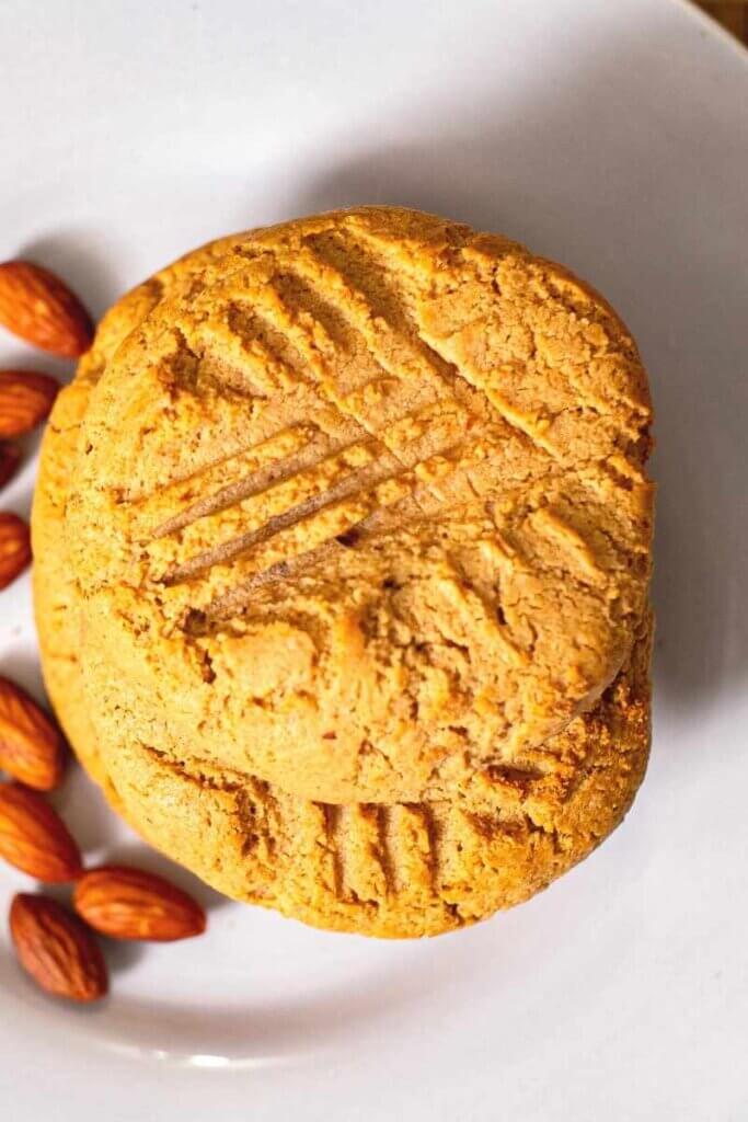 top shot of a stack of miso almond butter cookies next to almonds on white plate