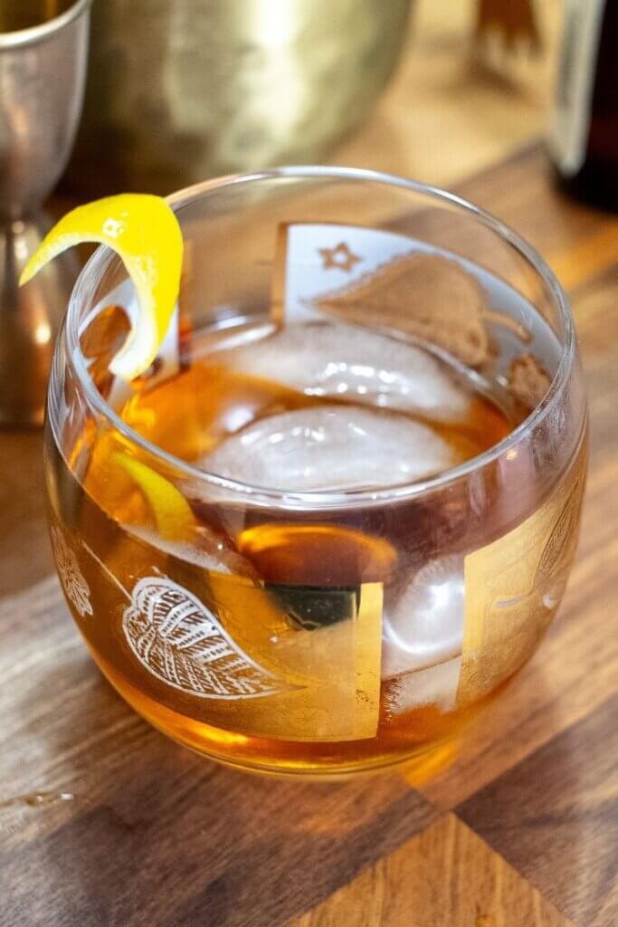 close up of honey old fashioned in a low ball glass with lemon twist