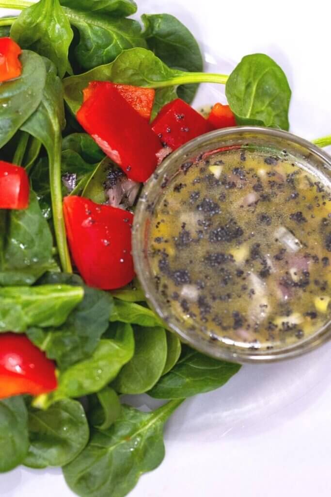 a bowl of vegan poppy seed dressing on a plate with salad