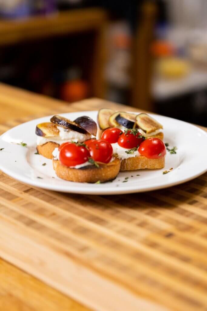 whipped ricotta crostini topped with tomatoes on a white plate