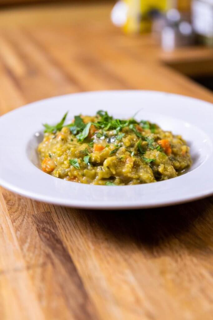 vegan split pea soup in a white bowl topped with garnish