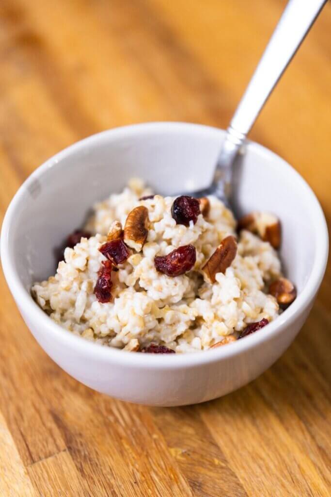 side view of coconut milk oatmeal in a bowl wtih nuts and dried fruit