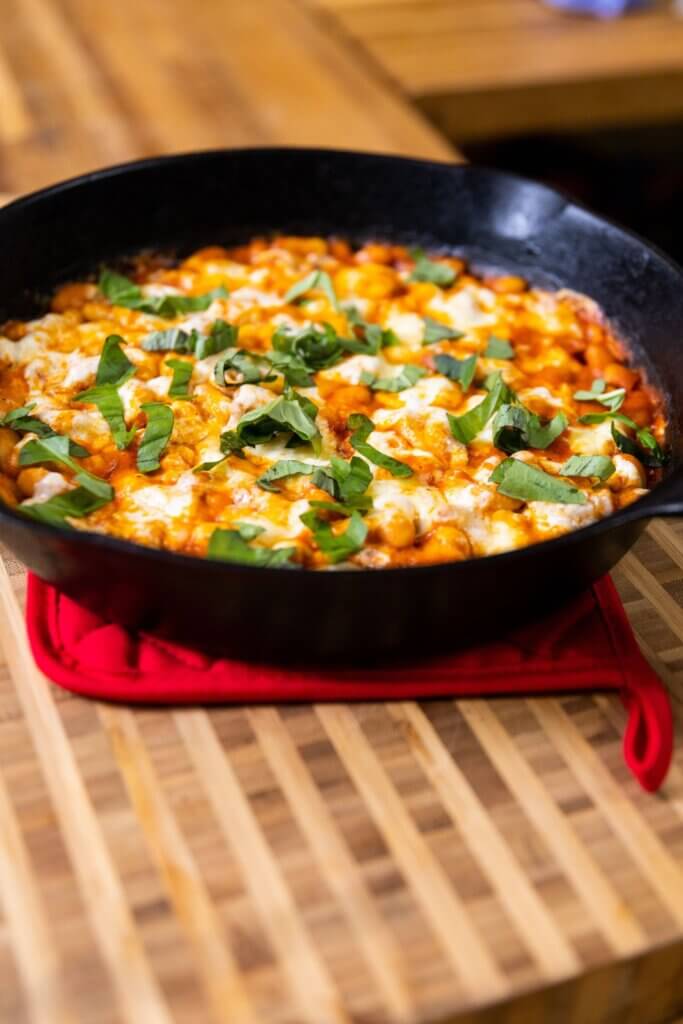 side view of cheesy white bean tomato bake on the counter in a cast iron skillet