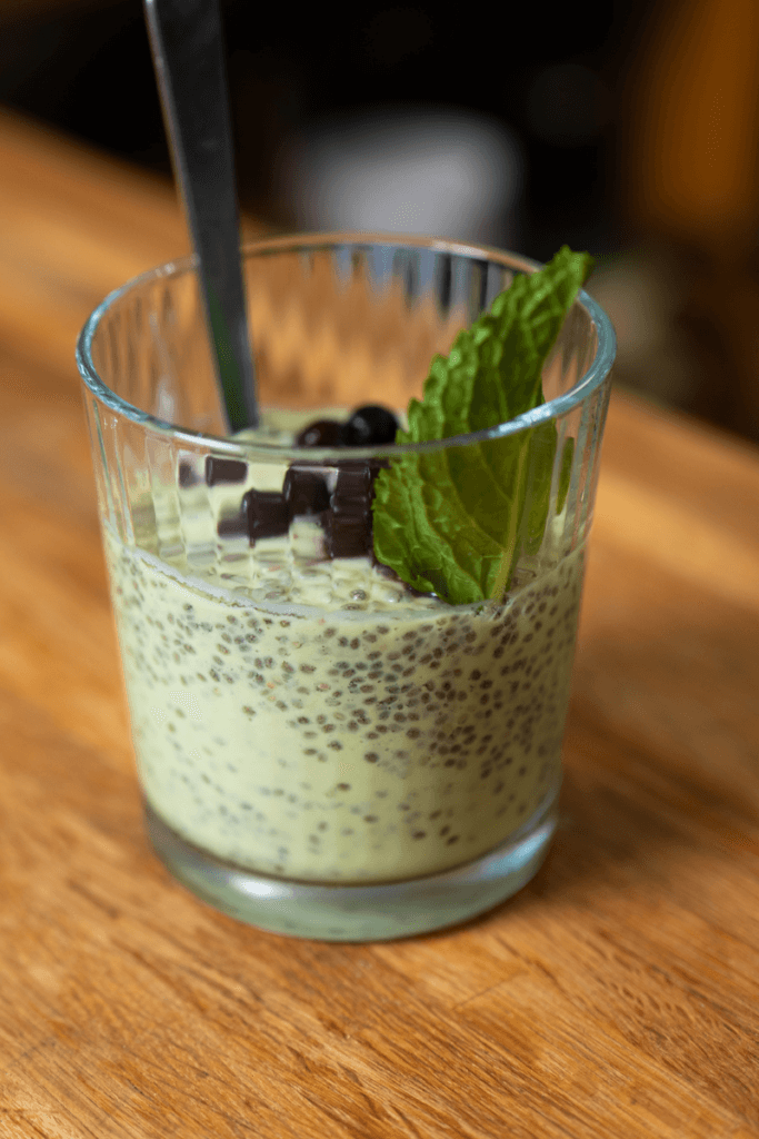 side view of a glass of avocado chia pudding topped with berries and a mint leaf.