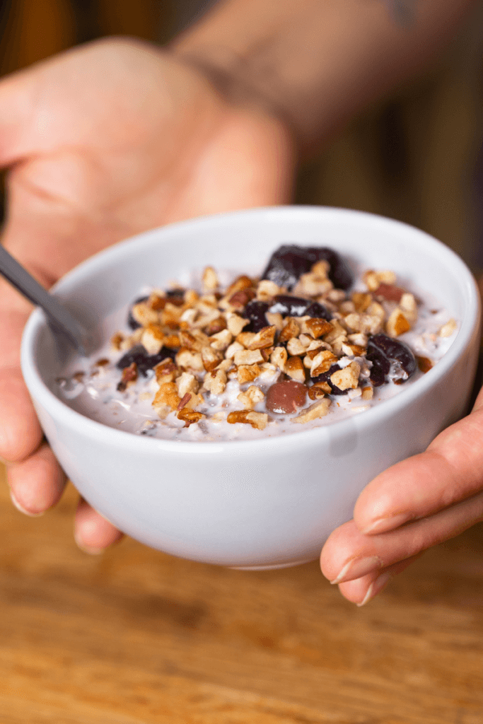holding a bowl of overnight cherry oats with nuts on top.