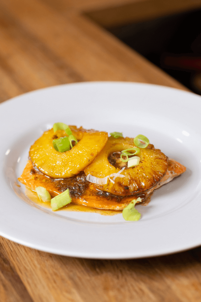 A filet of honey jerk salmon topped with two pineapple rings and glaze. 