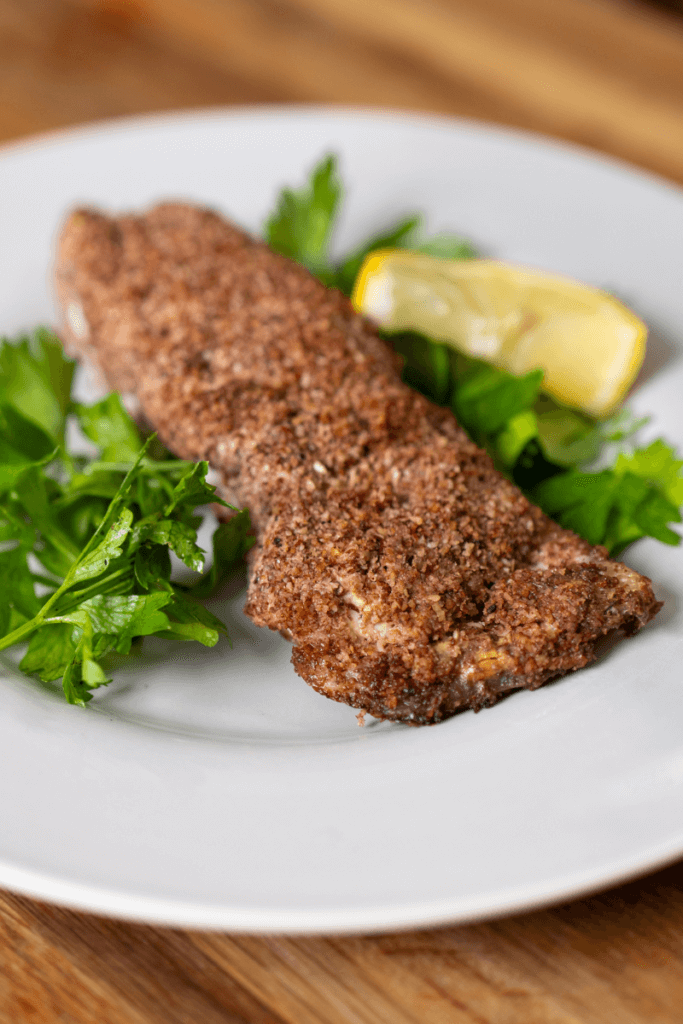 halibut coated in a pecan crust on a plate with a lemon slice. 