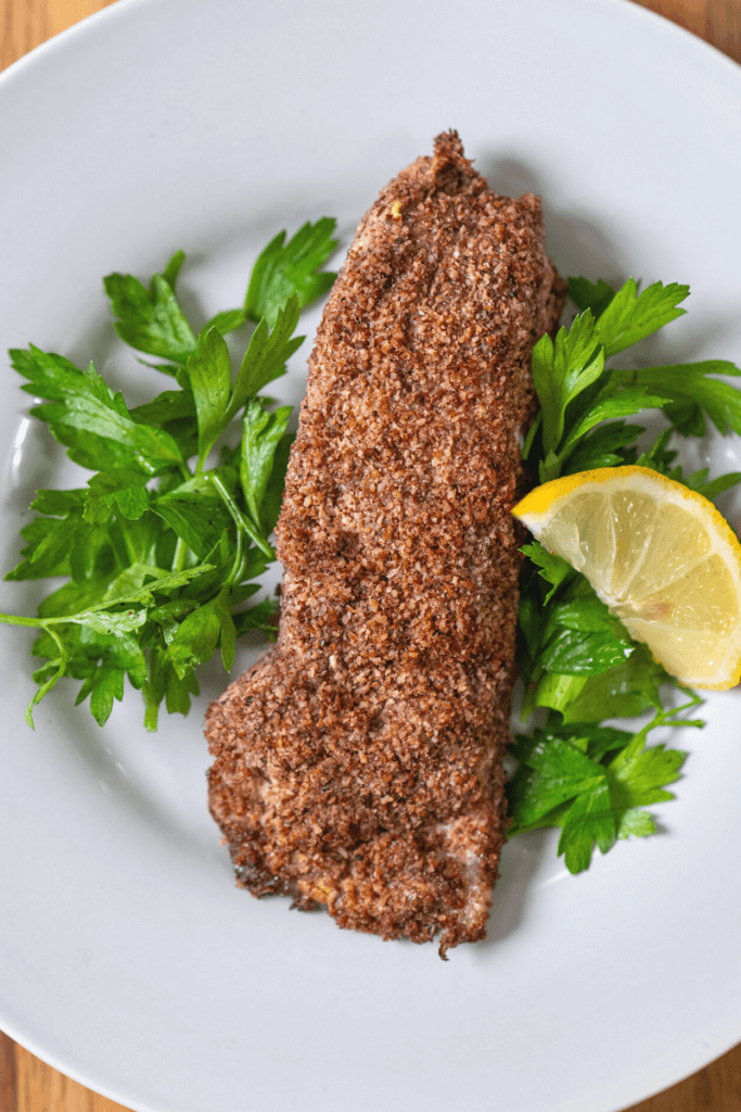 Pecan crusted halbut on a white plate with a lemon slice