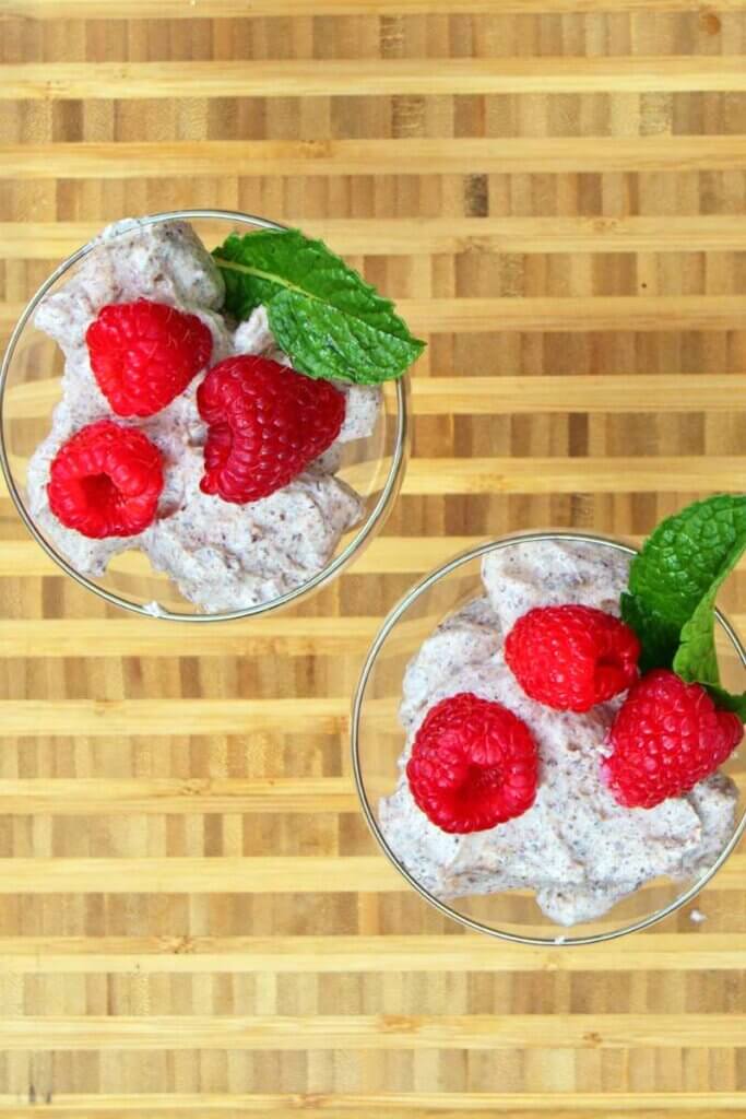 Top view of two glasses of chocolate ricotta mouse topped with mint and berries.