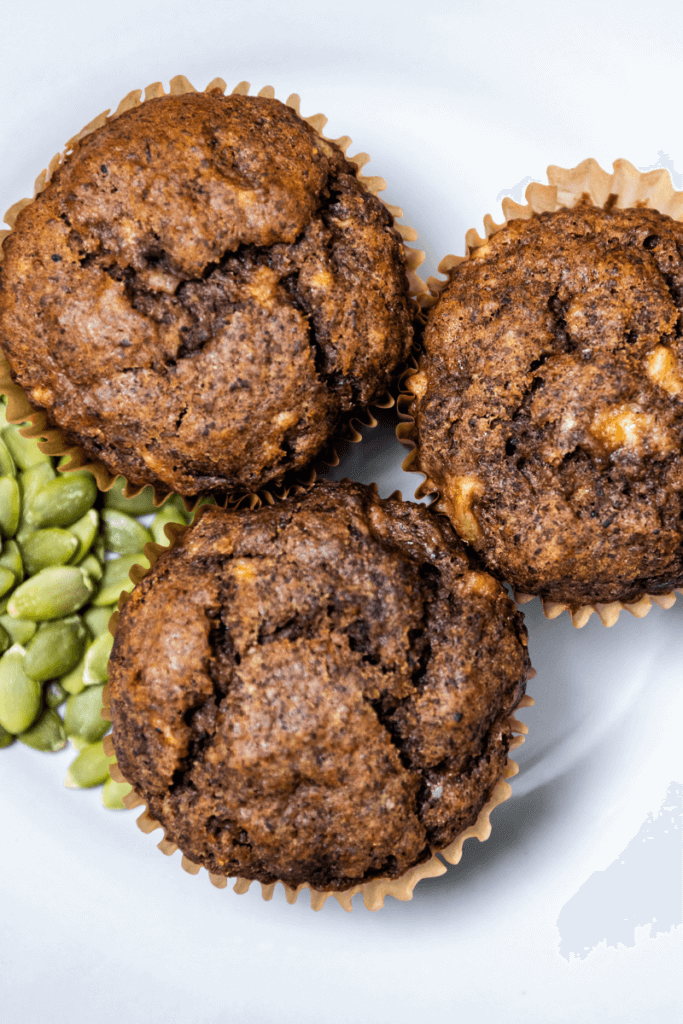 Three banana lentil muffins on a white plate next to green lentils.