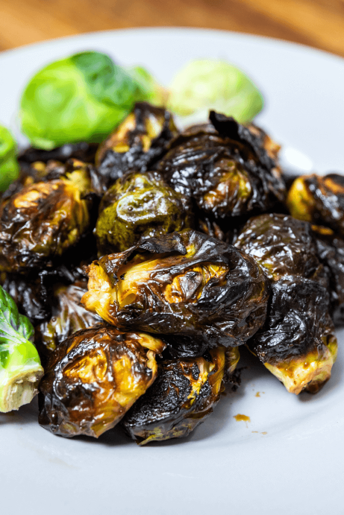Crispy Maple Balsamic Brussels Sprouts on a plate with raw sprouts.