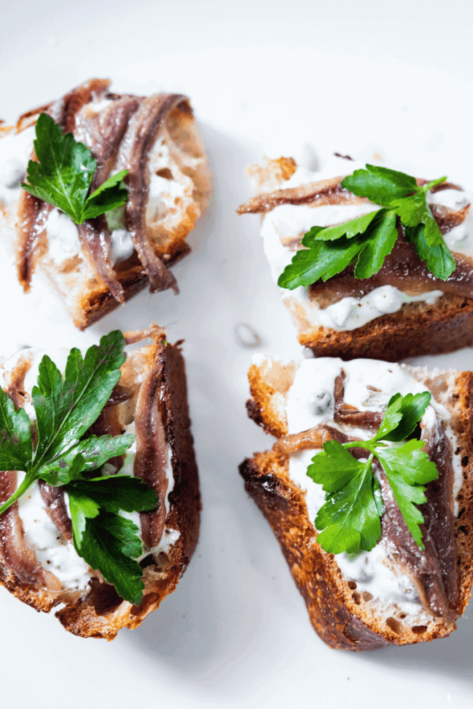Top view of homemade anchovy tapas on a large white plate.