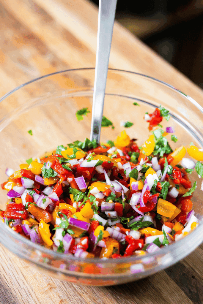 A bowl of red pepper salsa with a spoon in it.