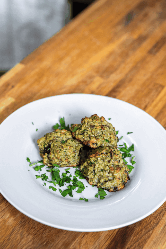 Three eggplant parmesan meatballs on a white plate garnished with parsley.