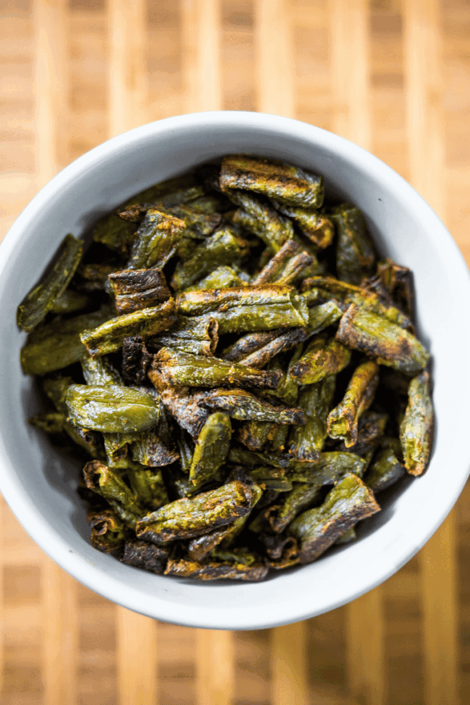 Top view of roasted frozen green beans in a white bowl.