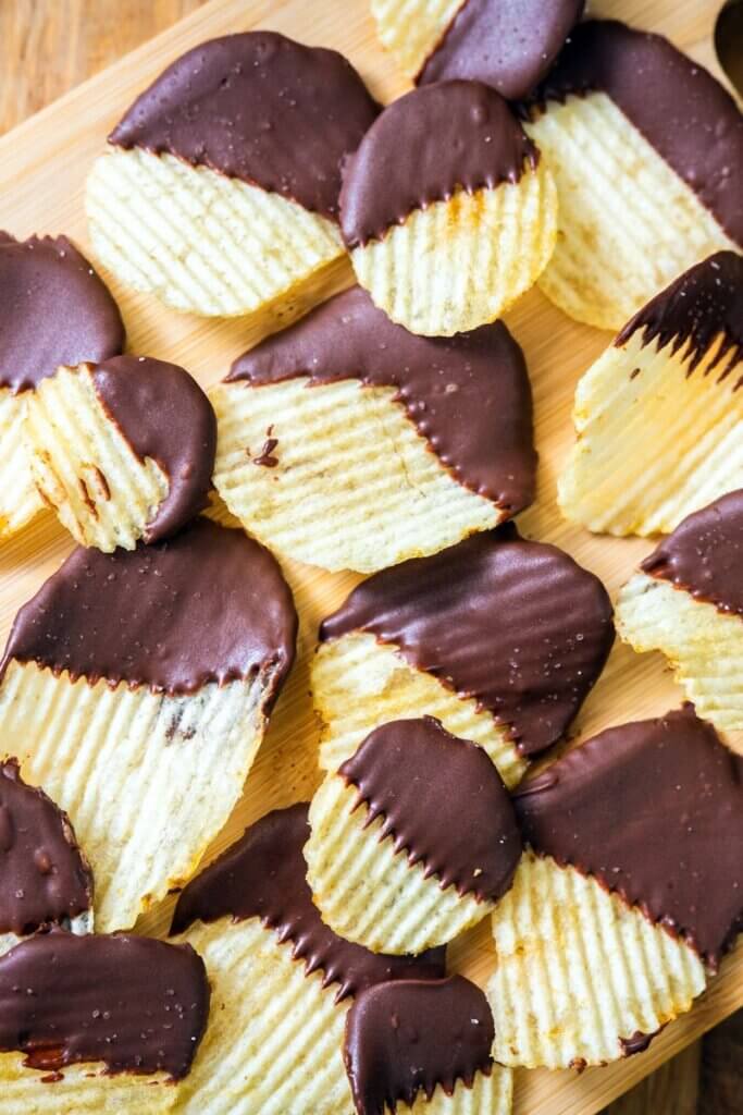Top view of chocolate covered potato chips on a wooden cutting board. 