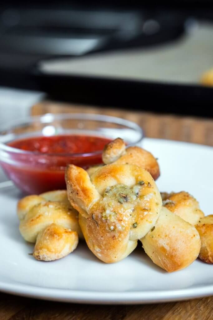 Sourdough garlic knots on a white plate with a bowl of marinara sauce.