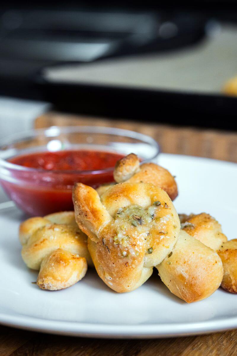 Sourdough garlic knots on a white plate with a bowl of marinara sauce.