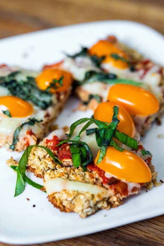 Three pieces of oatmeal flatbread topped with tomatoes and basil on a white plate.
