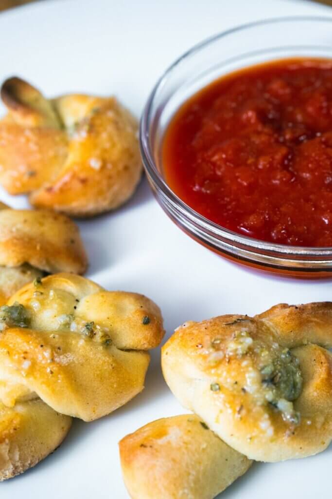 Homemade sourdough garlic knots on a white plate with marinara sauce.