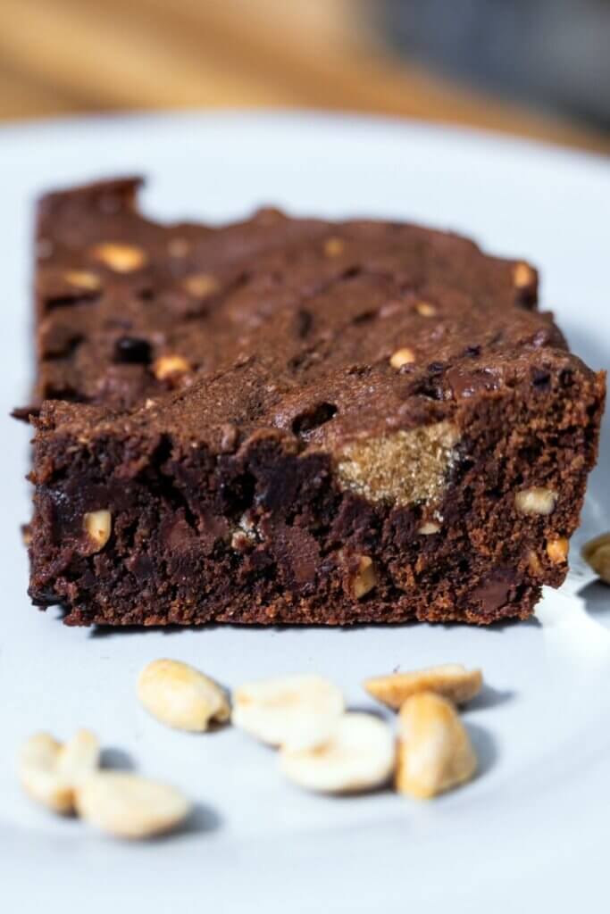 Homemade cocoa peanut butter brownie on a white plate next to peanuts.