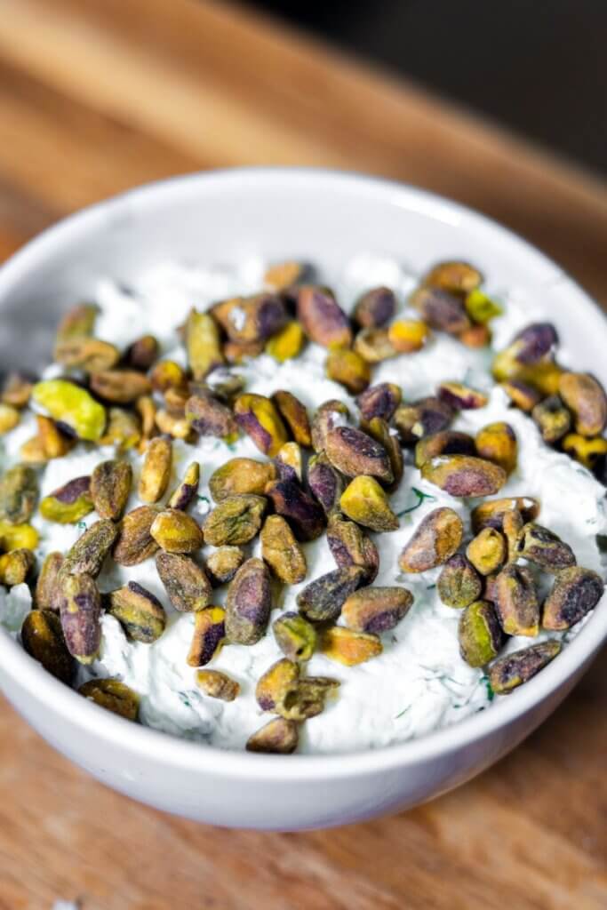 Pistachio cream cheese dip in a white bowl topped with extra pistachios.