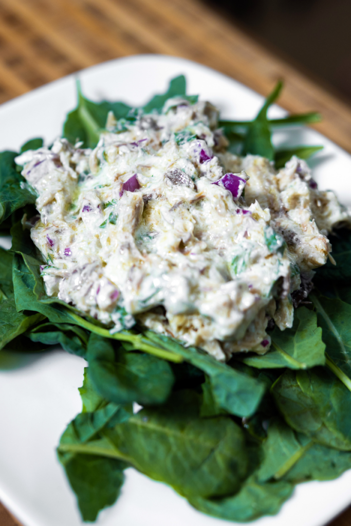 Smoked mackerel salad on a bed of greens on a white plate.