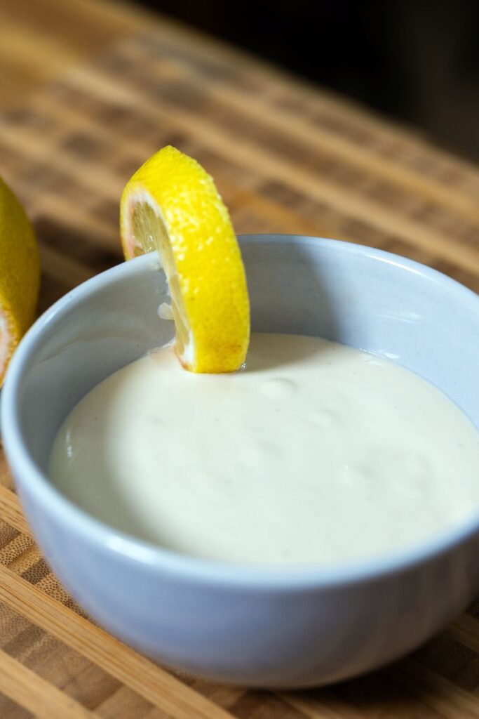 Homemade lemon tahini dressing in a white bowl with a lemon slice.