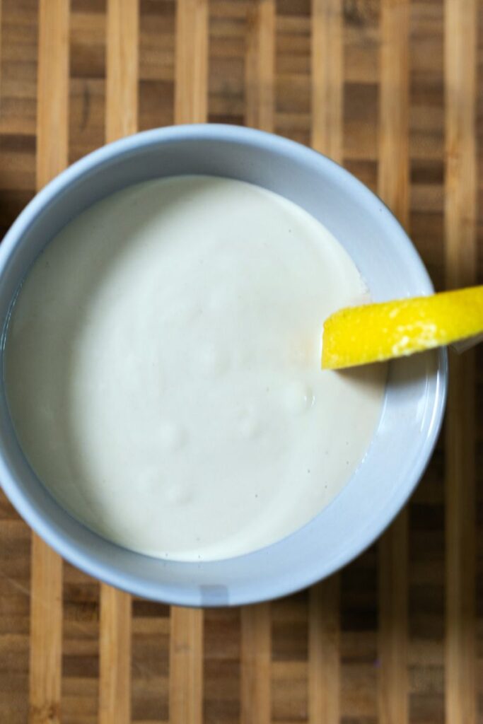 Top view of tahini lemon dressing in a white bowl with a lemon slice on the side.